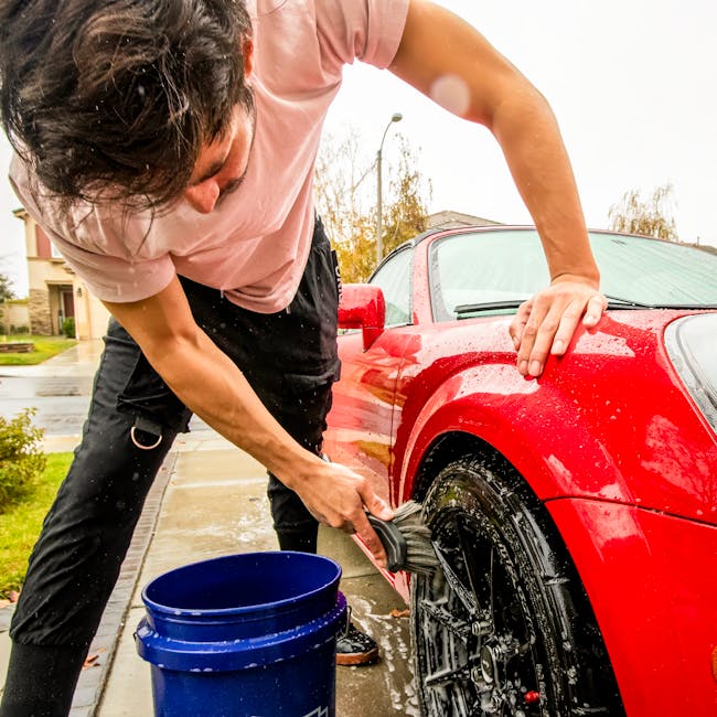 비오는 날 어른이 솔과 양동이를 이용해 빨간색 스포츠카 바퀴를 씻고 있다.